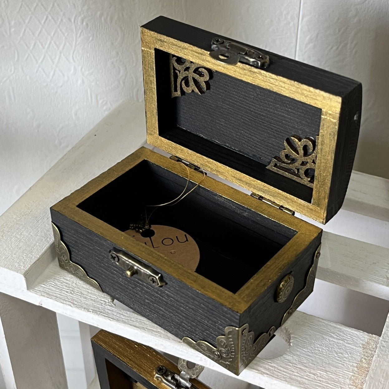 Decorative wooden gold and black ornate box with open lid.