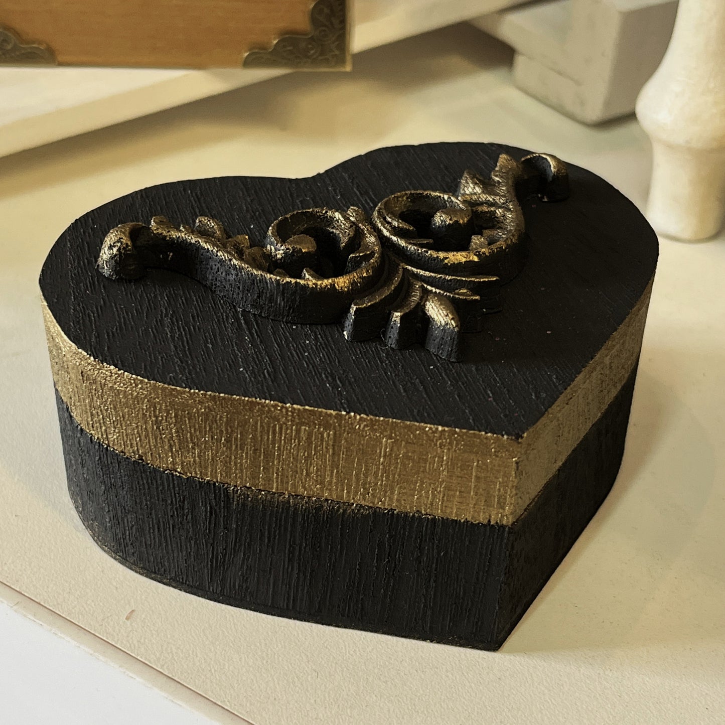 Heart-shaped wooden black and gold decorative box with intricate design gold motif design on lid.